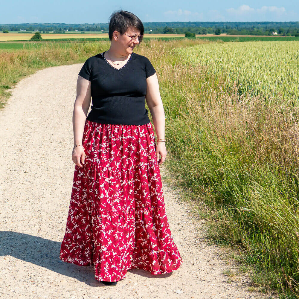 Femme portant une jupe bohème Mirabelle rouge à fleurs sur un chemin rural, taille élastiquée, idéale pour la couture.