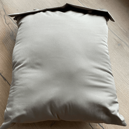 Coussin décoratif en tissu beige sur une surface en bois, avec une apparence douce et élégante.