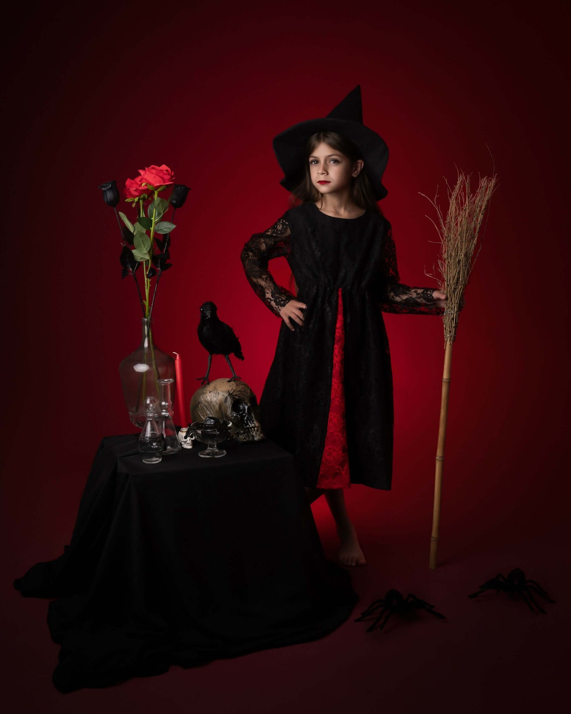 Petite fille en déguisement de sorcière noire avec chapeau, devant une table décorée pour Halloween.