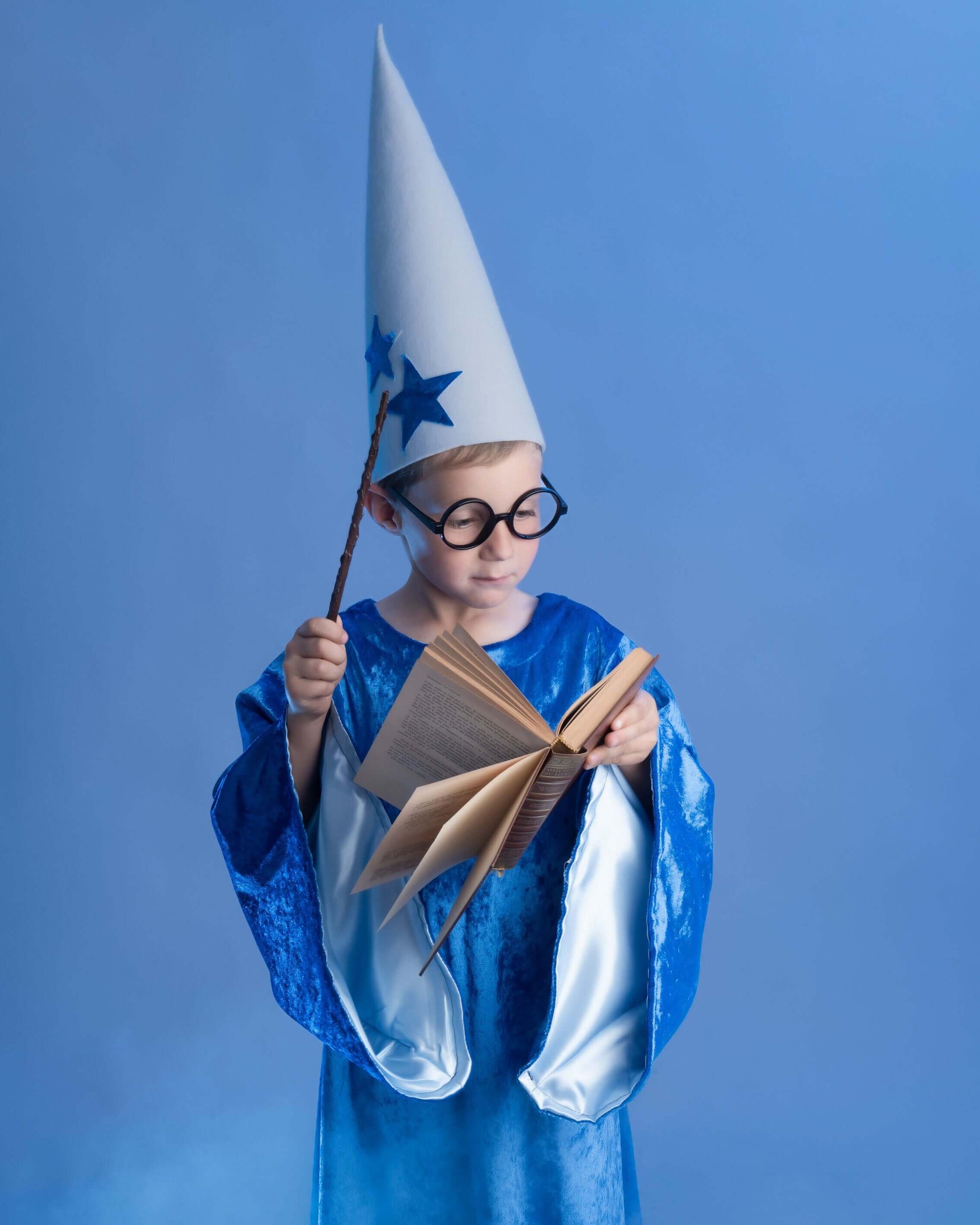 Enfant portant un déguisement d'apprenti sorcier avec chapeau, baguette et livre ouvert, sur fond bleu.