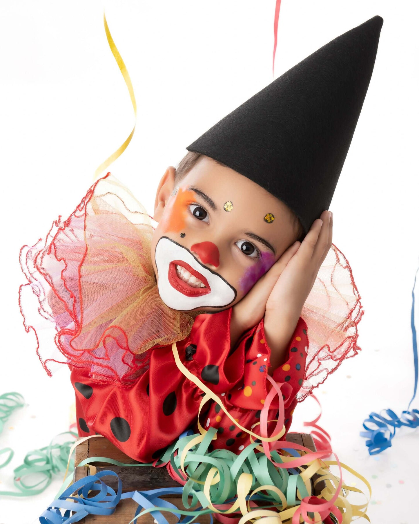 Enfant déguisé en clown avec chapeau pointu et collerette colorée, prêt pour le carnaval.