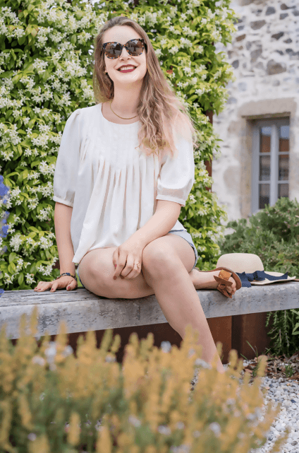 Mode féminine : femme souriante vêtue de la blouse ROSAE, posant en plein air entourée de fleurs.