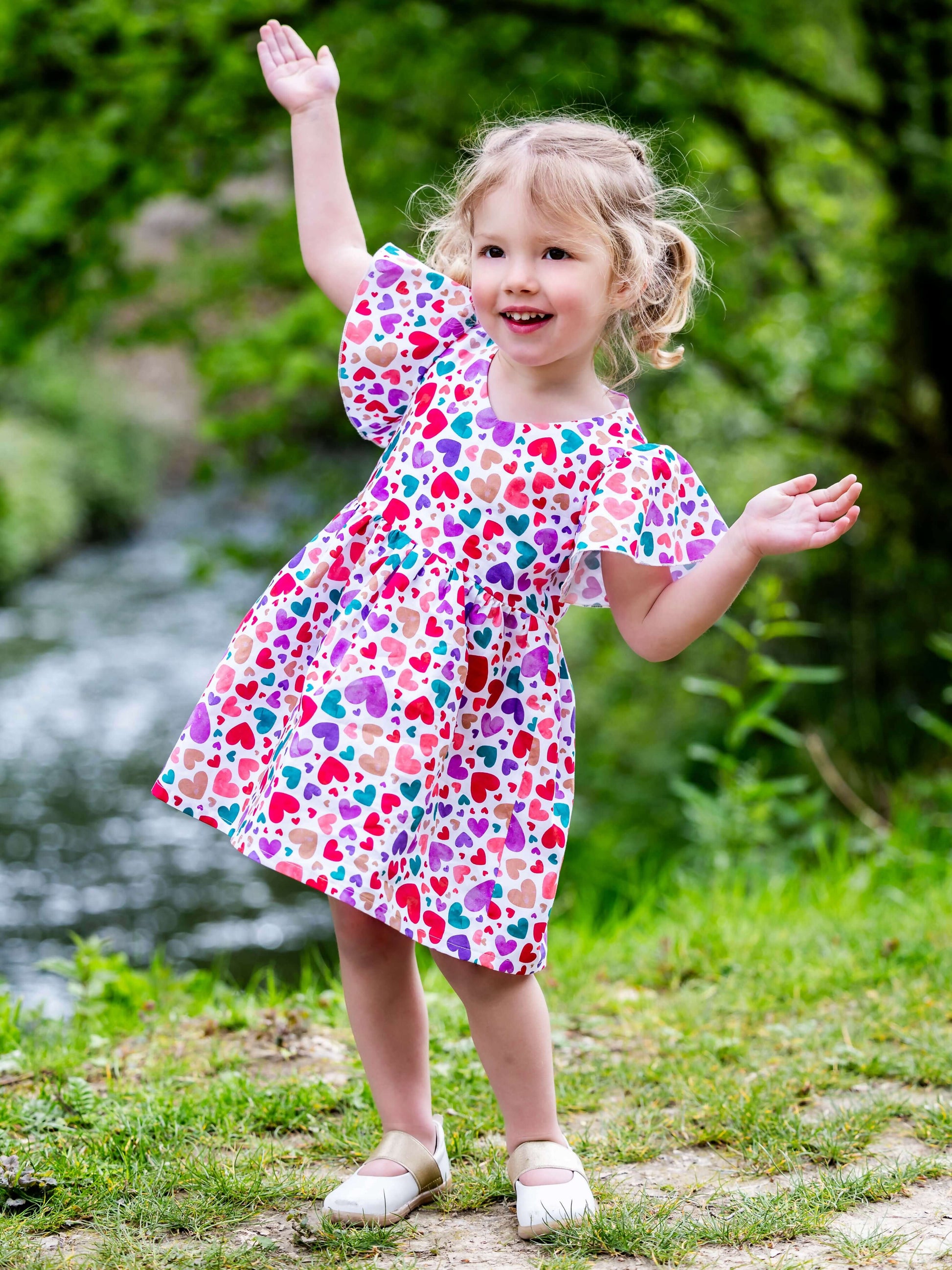 Enfant souriante portant la robe colorée Airelle au bord d'un ruisseau, patron de couture pdf à télécharger, AIRELLE - La robe / blouse aux 1000 versions.