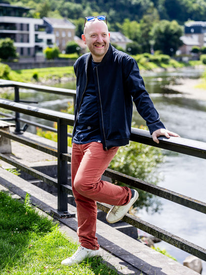 Homme portant AMANDE : le bomber noir, stylé et confortable, au bord d'une rivière. Patron de couture pdf à télécharger disponible.