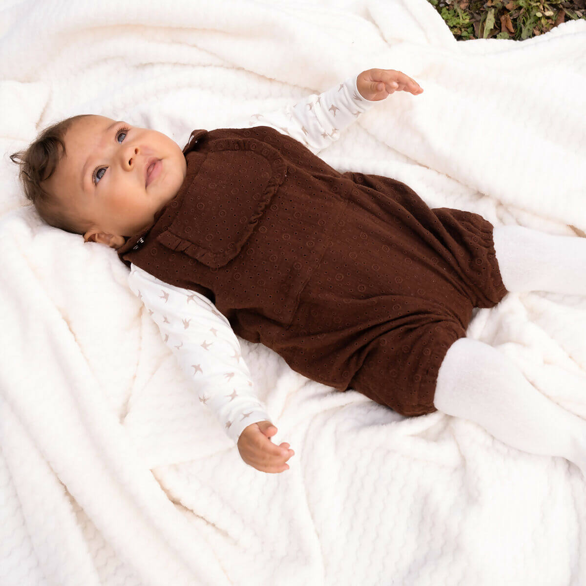 Bébé dans la BERGAMOTE - La combinaison aux 54 versions, patron de couture pdf à télécharger, allongé sur une couverture blanche.