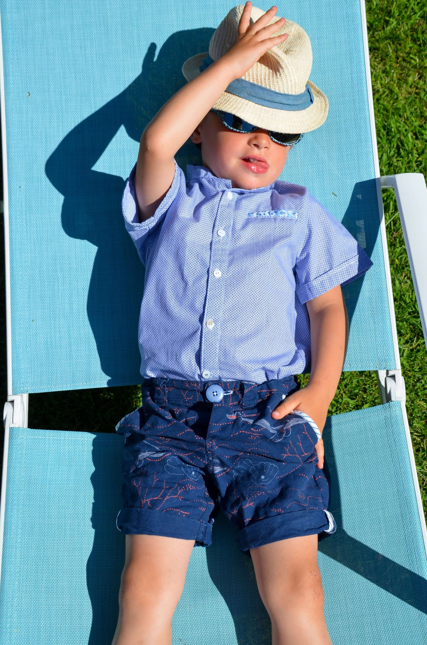 Enfant portant une chemisette et un bermuda, relaxant au soleil sur un transat, parfait pour l'été.