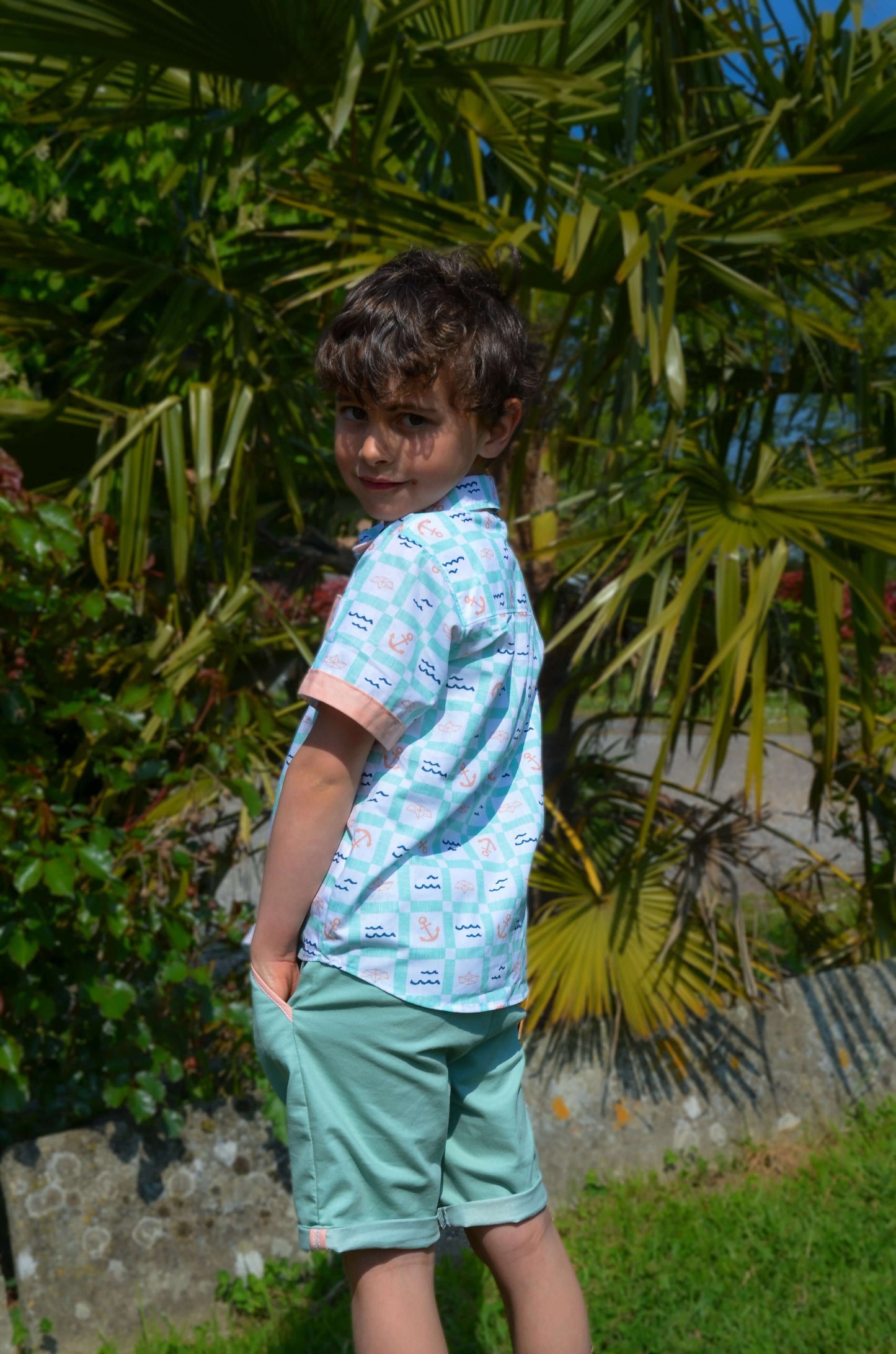 Enfant portant un bermuda Basalte et une chemisette colorée, en arrière-plan de verdure tropicale.