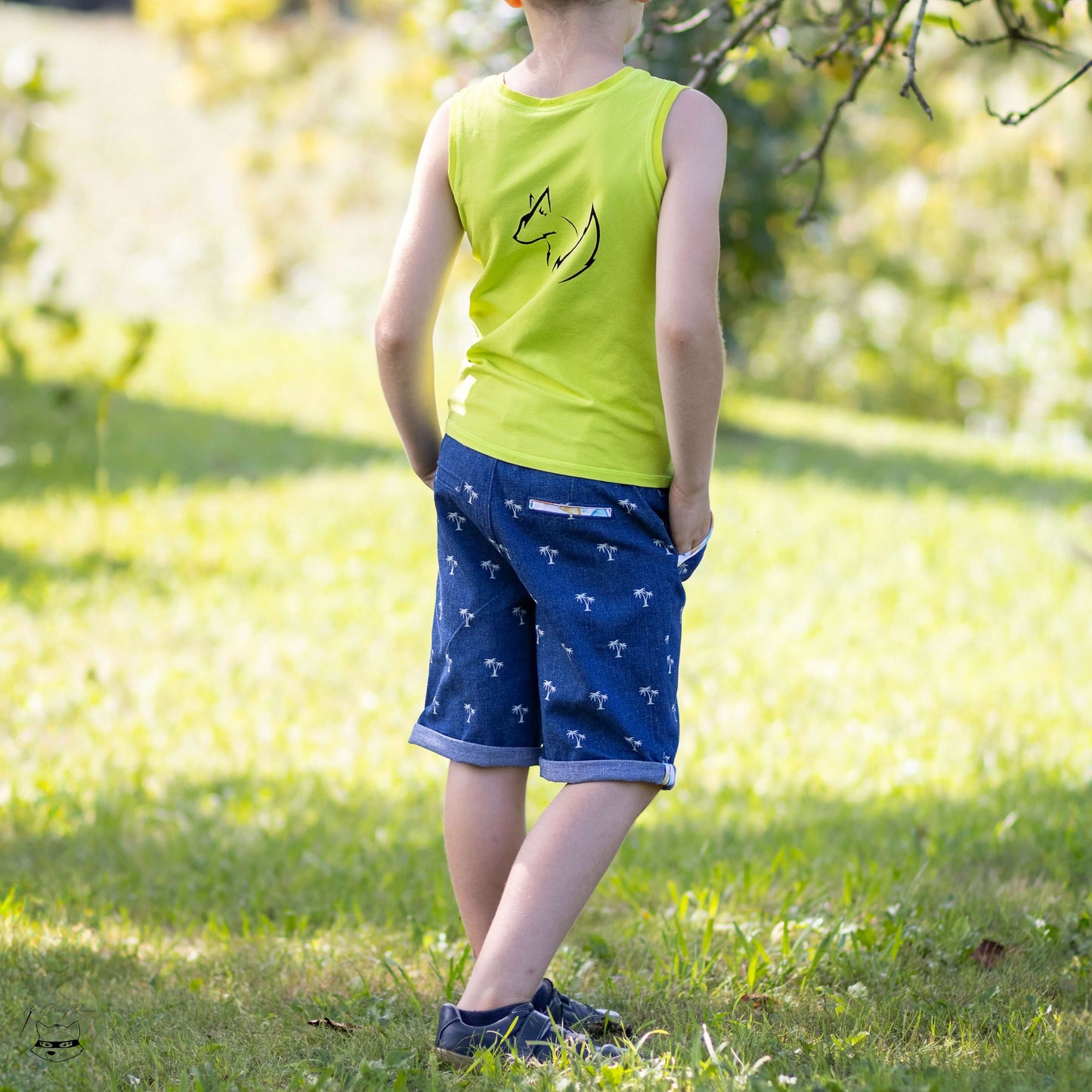 Enfant portant un bermuda BASALTE et un débardeur vert, profitant d'une journée ensoleillée en extérieur.