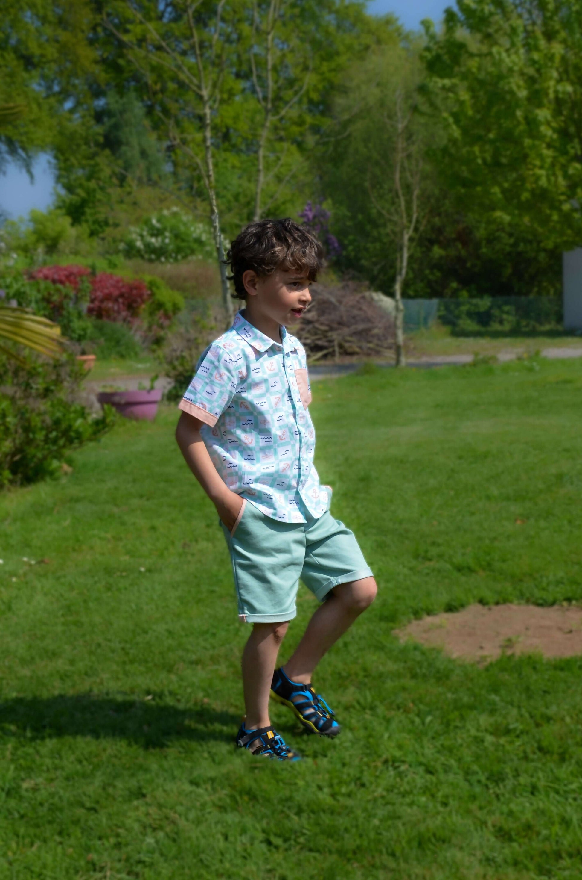 Enfant portant un bermuda BASALTE avec chemisette dans un jardin ensoleillé, look décontracté et stylé.