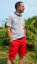 Homme en bermuda rouge tendance avec polo gris, style décontracté en été, parfait pour un look élégant.