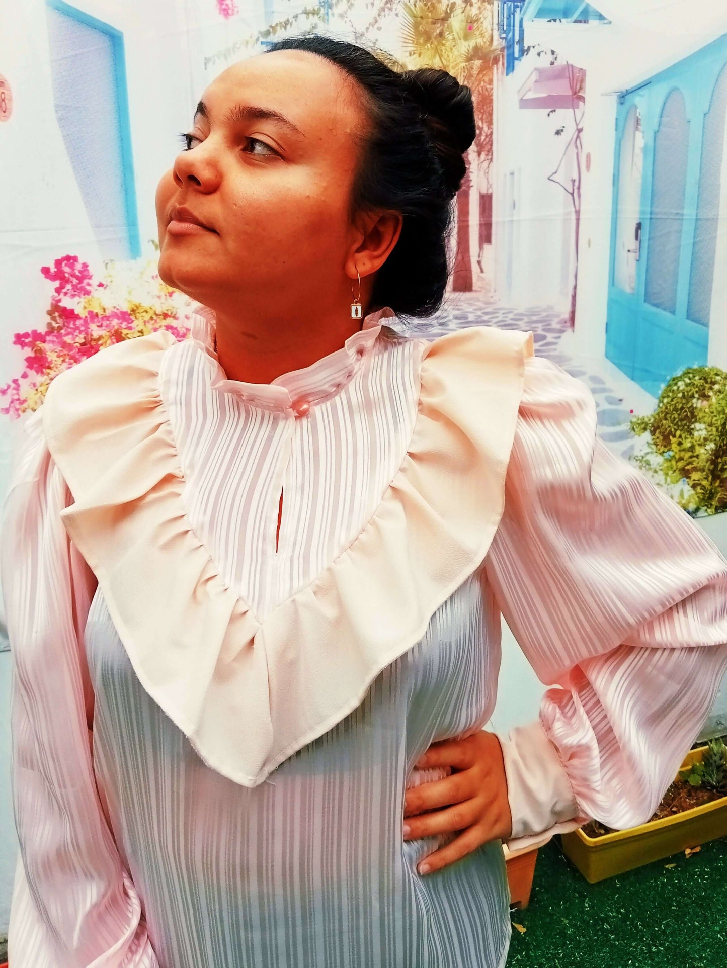 Femme portant une blouse à col monté froncé et volants, avec un arrière-plan coloré et vivant.