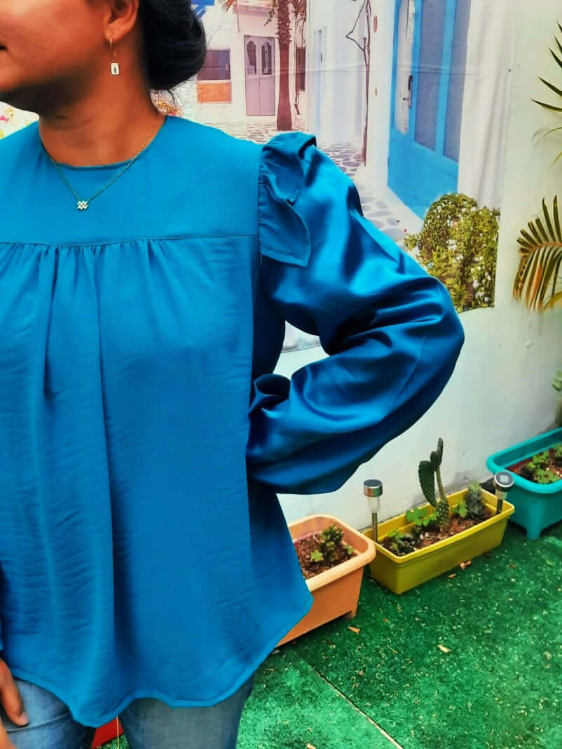 Blouse Idunn en satin bleu avec volants, collier simple, et ambiance colorée, idéale pour un patron de couture à télécharger.