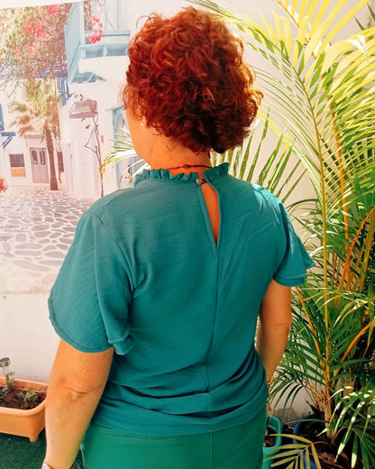 Femme portant une blouse verte à col montant froncé, vue arrière, avec fente décorative et ambiance estivale.