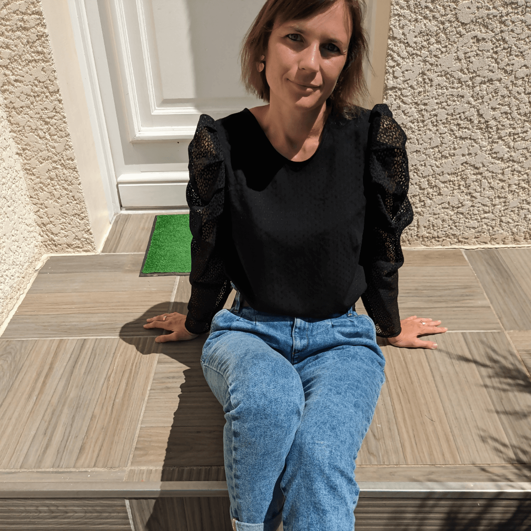 Femme portant la Blouse Quetzal | Taille 32 à 50, assise sur des marches, mettant en valeur le patron de couture pdf à télécharger.