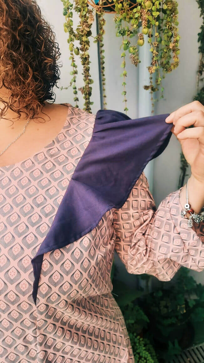 Femme tenant un volant violet de la blouse Thalie en tissu, mise en avant des détails de couture élégants.