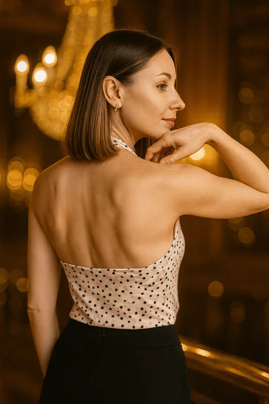 Femme portant un top sans manches à pois, vue de dos, dans un cadre élégant avec des lumières en arrière-plan.