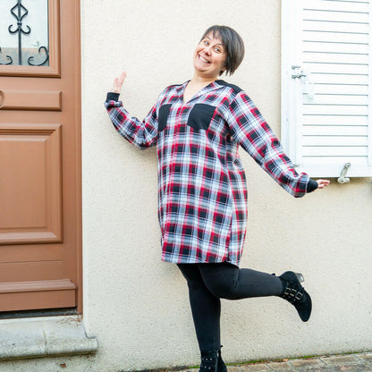 Femme souriante en blouse rouge à carreaux, style chemise, posant devant une porte.