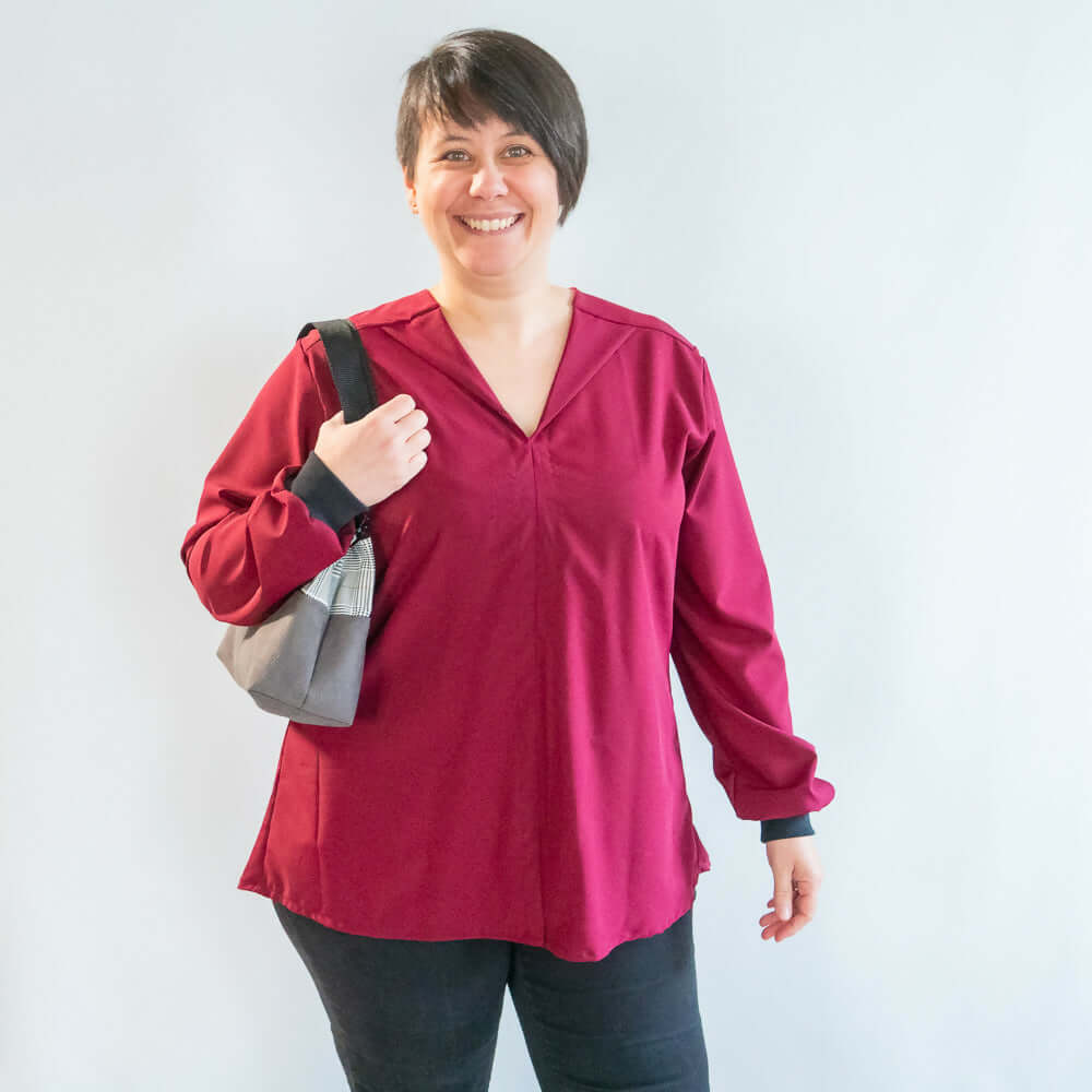 Femme souriante portant une blouse robe Myrtille, à manches longues, couleur bordeaux, avec un sac à main.