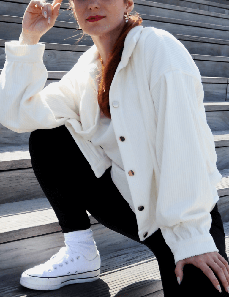 Femme portant un blouson Cosmos blanc décontracté sur des escaliers, exprimant son style personnel en couture.