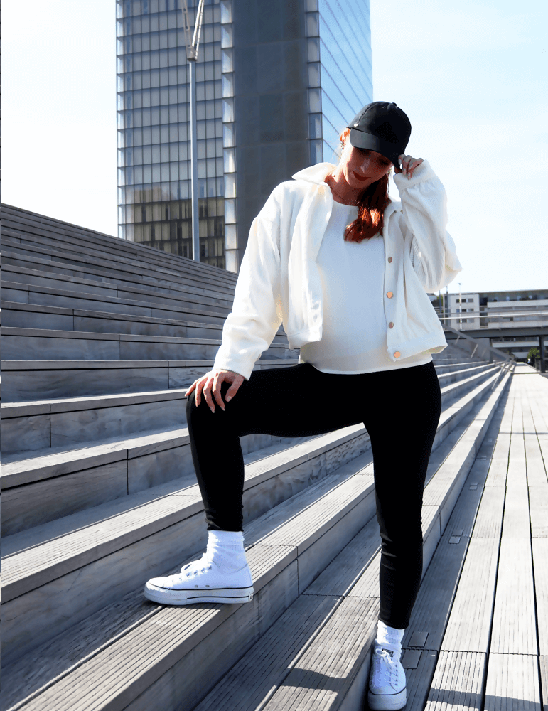 Femme posant sur des marches en blouson Cosmos blanc, look décontracté avec un style moderne et sneakers.