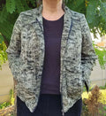 Femme portant le Patron PDF Bomber Phoenix, vue de dos en tricot gris chiné, dans un jardin verdoyant