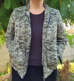 Femme portant le Patron PDF Bomber Phoenix, vue de dos en tricot gris chiné, dans un jardin verdoyant