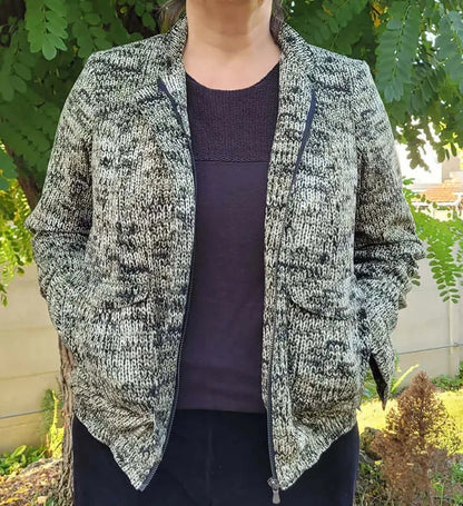 Femme portant le Patron PDF Bomber Phoenix, vue de dos en tricot gris chiné, dans un jardin verdoyant