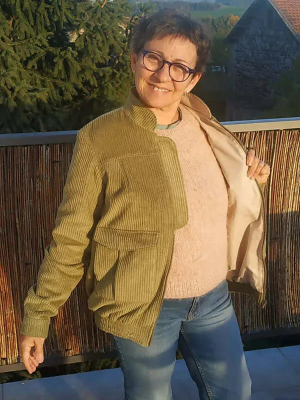 Femme portant le Patron PDF Bomber Phoenix en velours côtelé ocre, vue de face, sourire, terrasse avec vue campagne