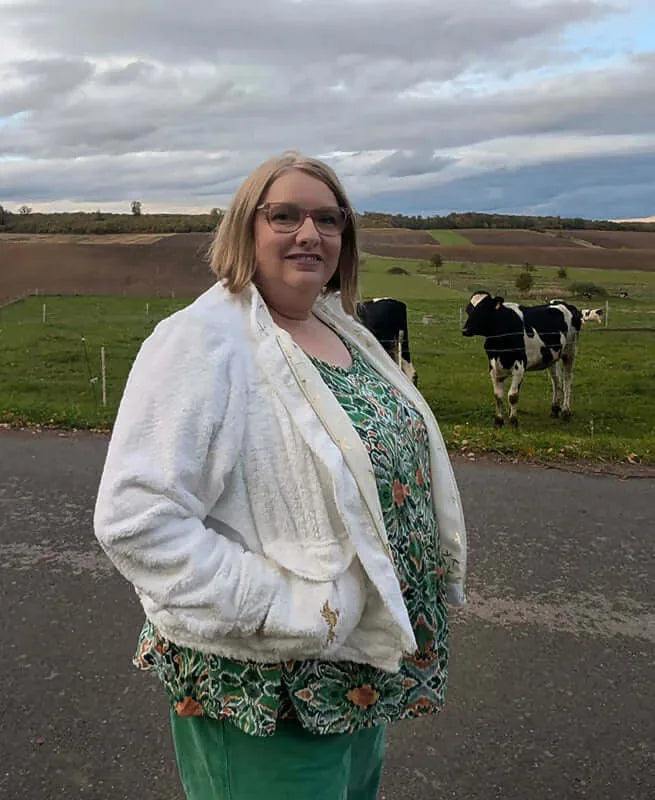 Femme portant le Patron PDF Bomber Phoenix, vue de face en vert et blanc, dans un paysage rural avec vaches