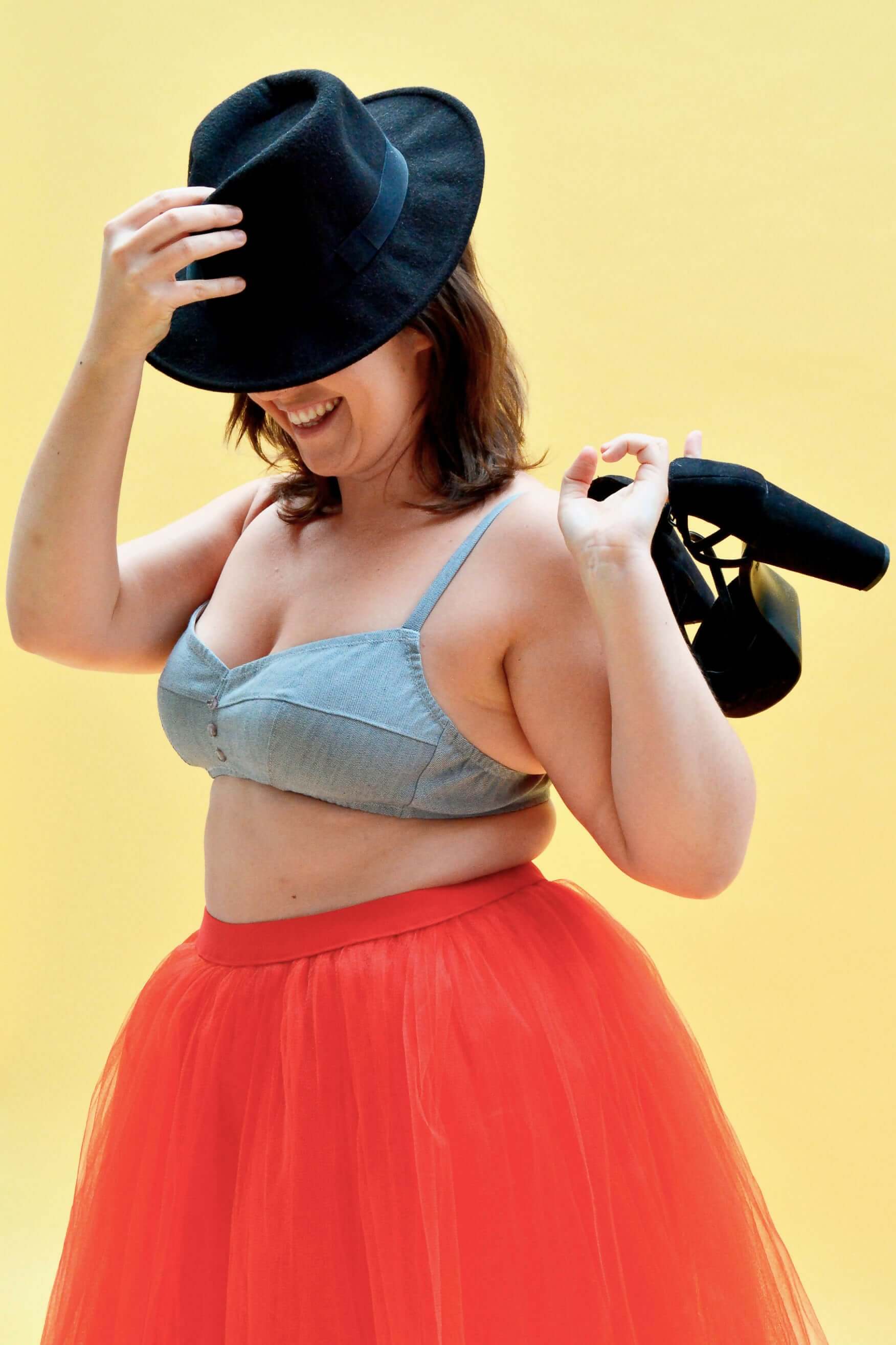 Femme souriante portant une brassière Curaçao et une jupe tulle rouge, avec un chapeau noir et des talons.