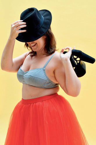 Femme souriante portant une brassière Curaçao et une jupe tulle rouge, avec un chapeau noir et des talons.