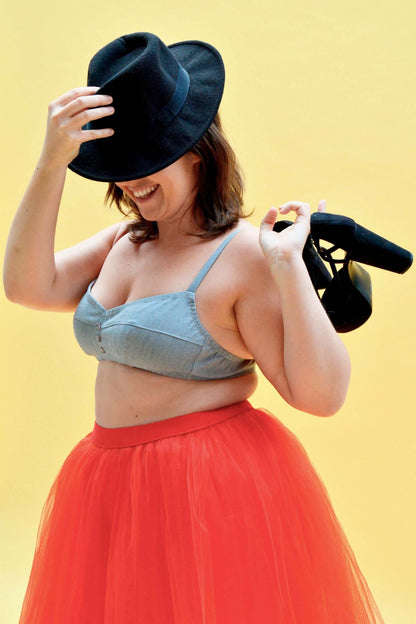 Femme souriante portant une brassière Curaçao et une jupe tulle rouge, avec un chapeau noir et des talons.