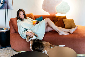 Femme en peignoir détendue sur un canapé avec chien, tenant une tasse, portant CANNELLE - Le pull-plaid, patron de couture pdf à télécharger.