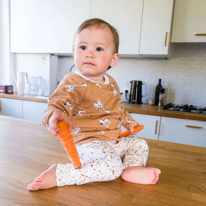Bébé portant CHATAIGNE - LE sweat aux 32 versions, patron de couture pdf à télécharger, assis sur une table de cuisine avec des carottes.