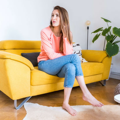 Femme portant CHATAIGNE - LE sweat aux 32 versions, assise sur un canapé jaune. Patron de couture pdf à télécharger.