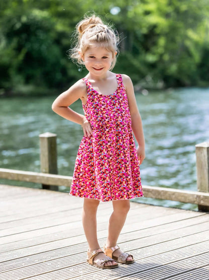 Petite fille portant CLEMENTINE - Le top et la robe d'été, patron de couture pdf à télécharger, au bord d'un lac ensoleillé.