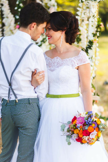 Couple de mariés élégants sous une arche florale, robe blanche et bouquet coloré en été