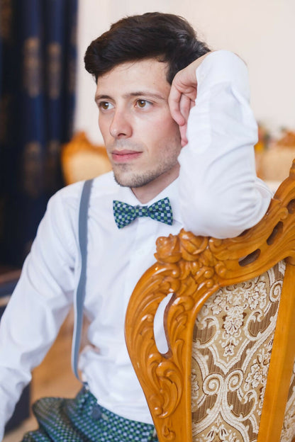 Homme assis sur une chaise en bois, portant une chemise blanche et un nœud papillon bleu, regard pensif.