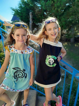 Deux filles portant des robes colorées avec des motifs d'animaux, souriant sur un escalier en extérieur.