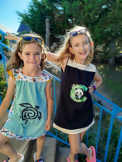 Deux filles portant des robes colorées avec des motifs d'animaux, souriant sur un escalier en extérieur.