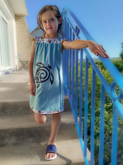 Jeune fille portant une robe d'été bleue avec motif tortue, sur un escalier extérieur.