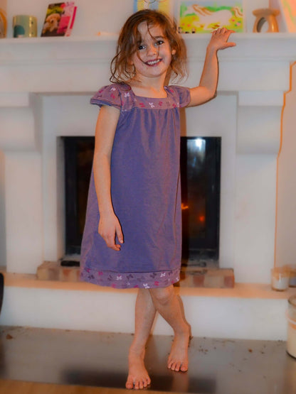 Enfant portant une chemise de nuit violette debout devant une cheminée, illustration pour patron de couture pdf à télécharger Chemise de nuit SONGE.
