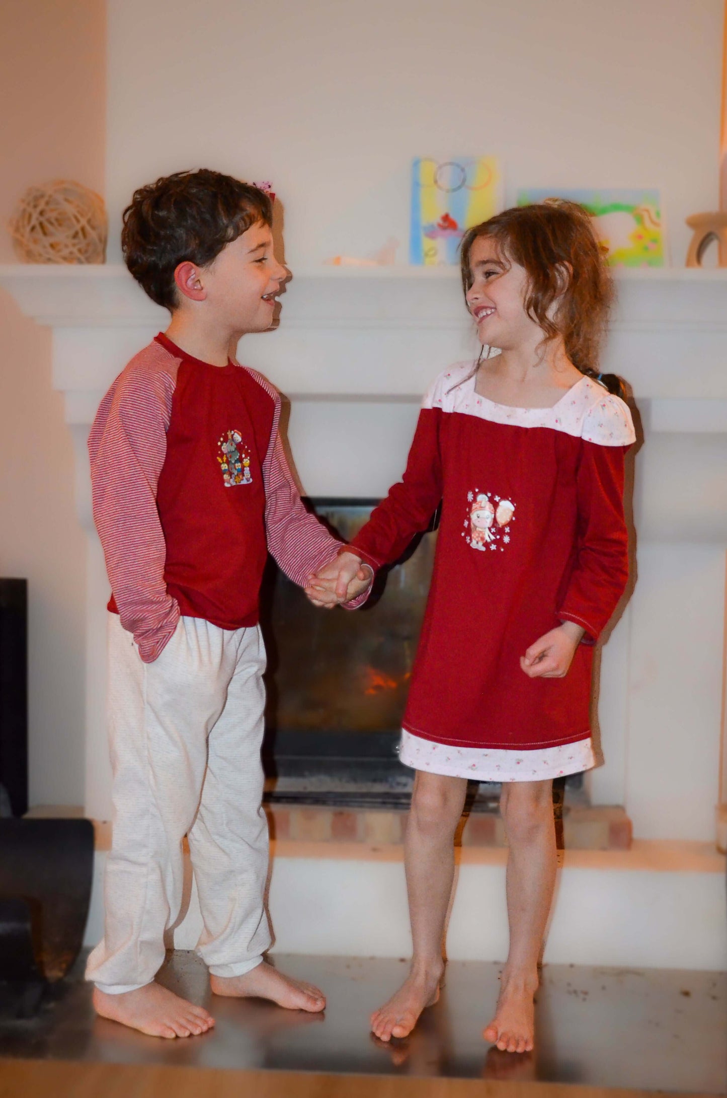 Enfants portant des vêtements assortis devant une cheminée, souriant et se tenant la main, ambiance chaleureuse et festive.