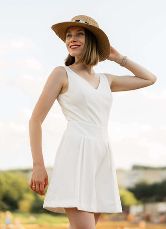 Femme en robe d'été blanche avec chapeau de paille dans un champ, souriante sous un ciel ensoleillé.