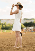 Femme en robe blanche et chapeau sur la plage, regardant en arrière