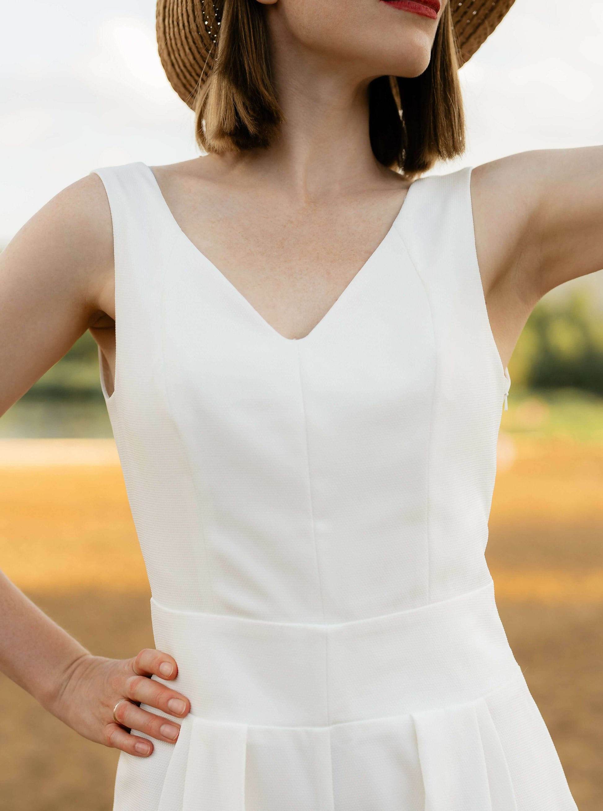Femme portant une robe blanche élégante avec un chapeau en plein air, captant l'esprit de la mode estivale décontractée et chic.
