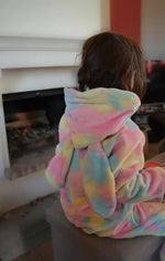 Enfant vêtu de la Combinaison/Surpyjama PAPILLOTE, couleurs pastel, assis près d'une cheminée. Patron de couture PDF à télécharger.