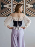 Femme portant un Corset - XS/L - CARMEN, patron de couture pdf à télécharger, vue de dos avec un corset noir et une blouse blanche.