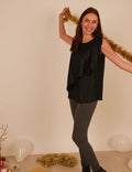 Femme souriante portant le débardeur Cara noir, élégant et décontracté, avec des leggings gris, en arrière-plan festif.