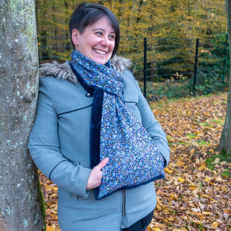 Femme souriante portant une écharpe avec manchon Baie rose dans un décor automnal, alliant confort et style.